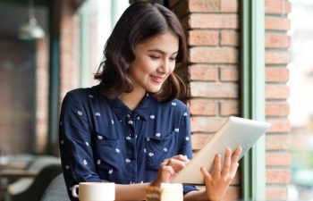 Joyful young woman using a tablet while having a coffee in a coffee shop.