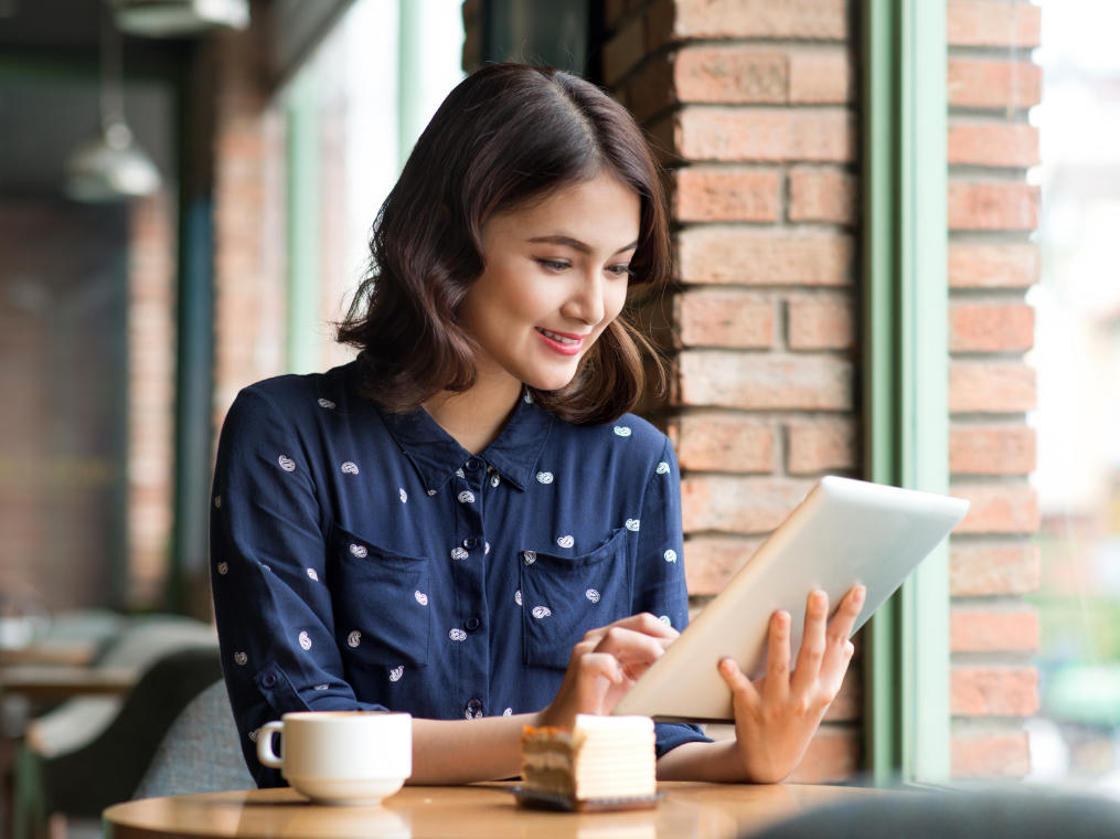 Joyful young woman using a tablet while having a coffee in a coffee shop.