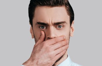 A concerned young ,man covering his mouth with a hand due to bad breath.