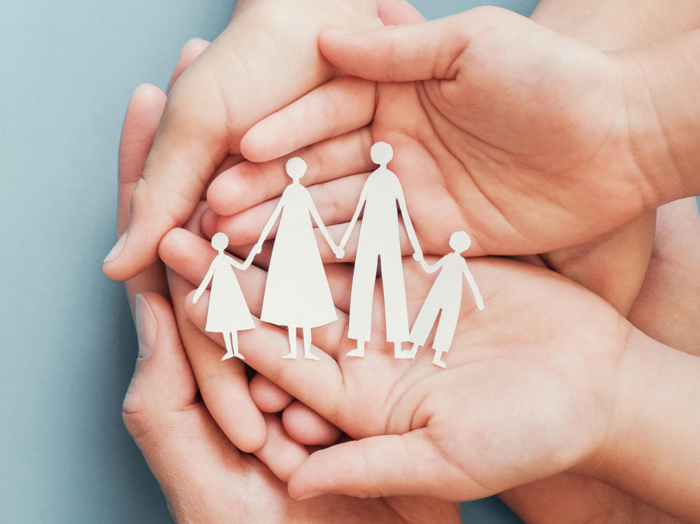 Open hands of an adult and a child holding paper figures showing parents with two children.